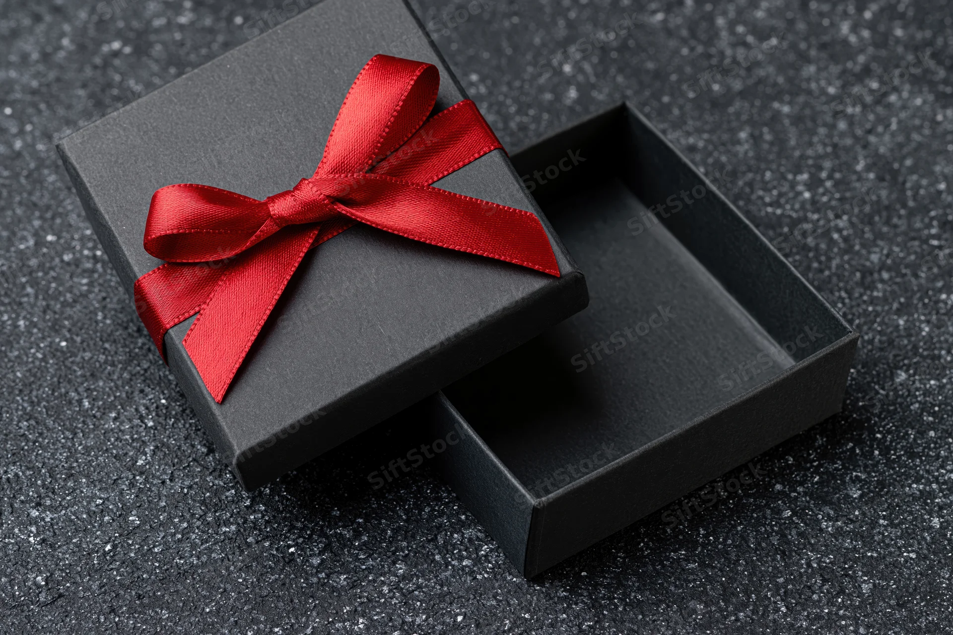 Open matte black gift box with red satin bow on dark textured surface
