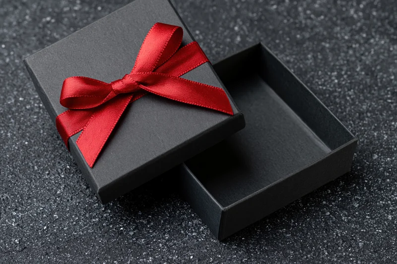 Open matte black gift box with red satin bow on dark textured surface