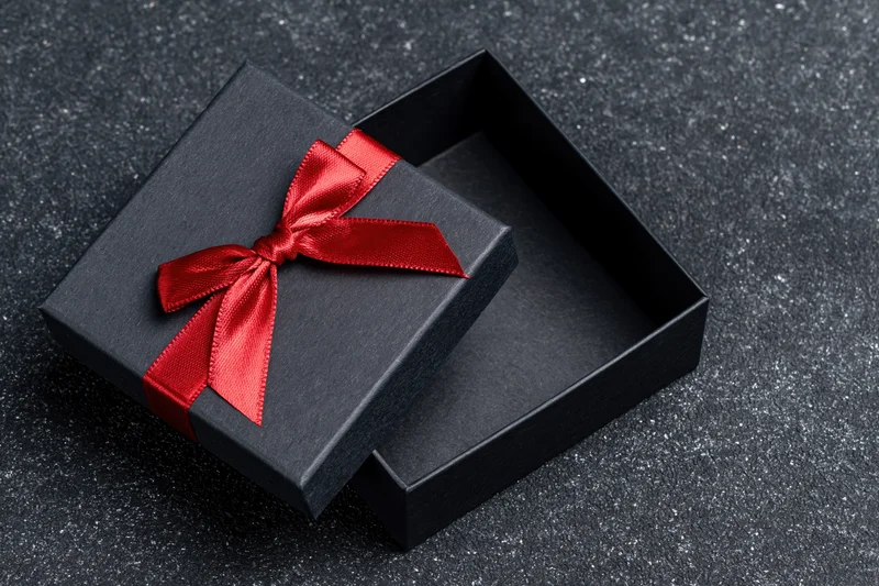 Open matte black gift box with red satin ribbon bow on dark textured surface