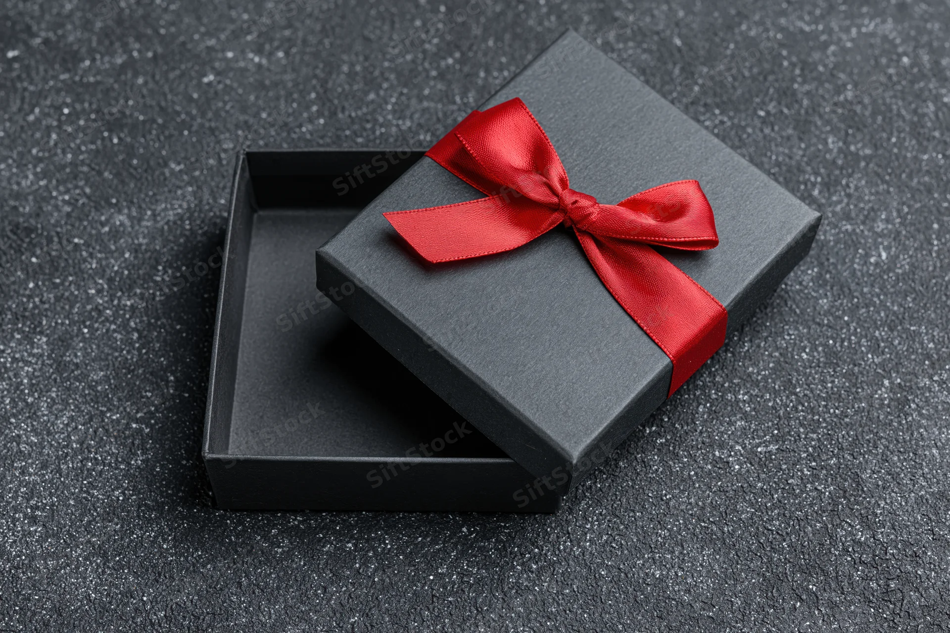 Open matte black gift box with red satin bow on textured dark surface