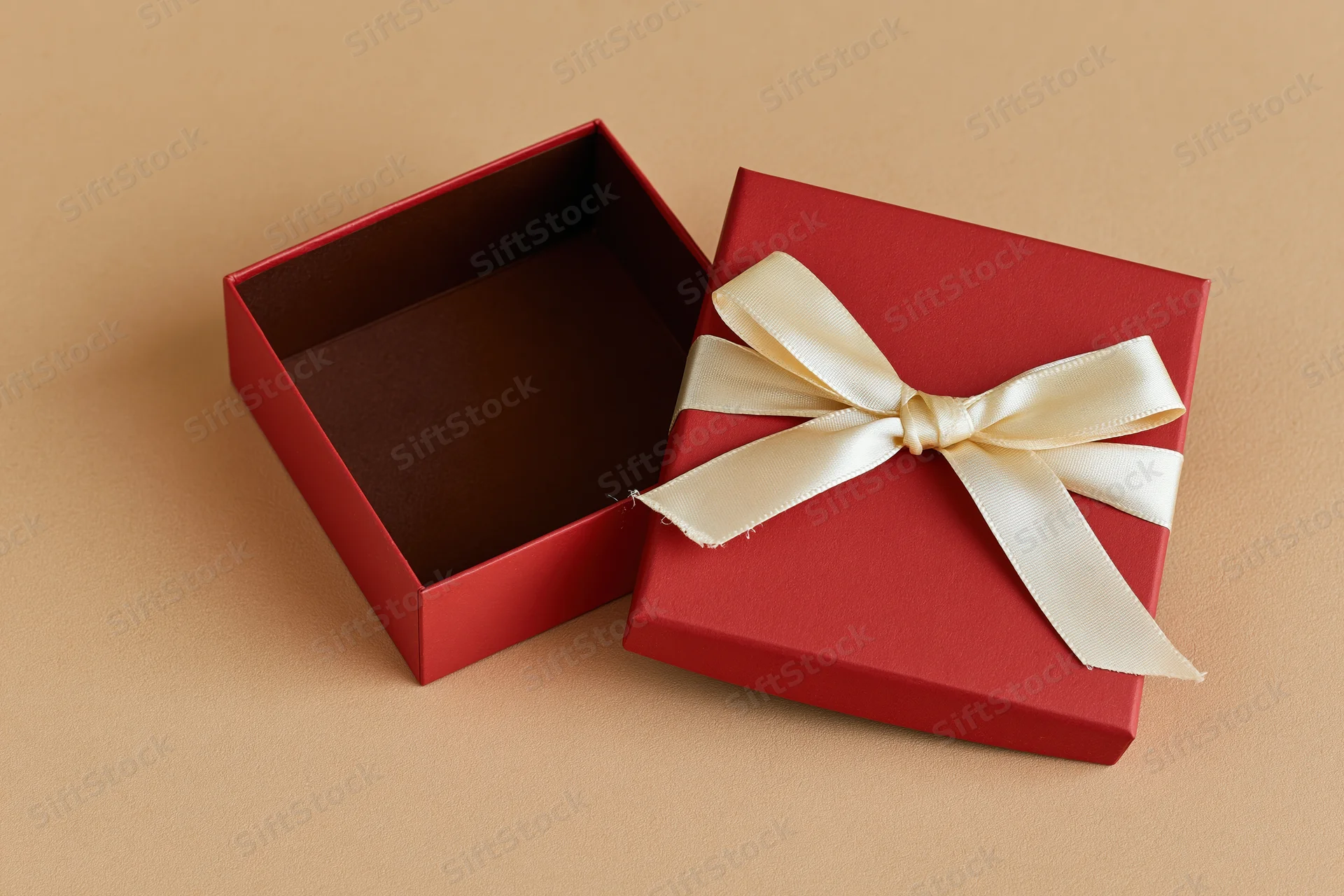 Open red gift box with cream ribbon bow beside its lid on beige surface