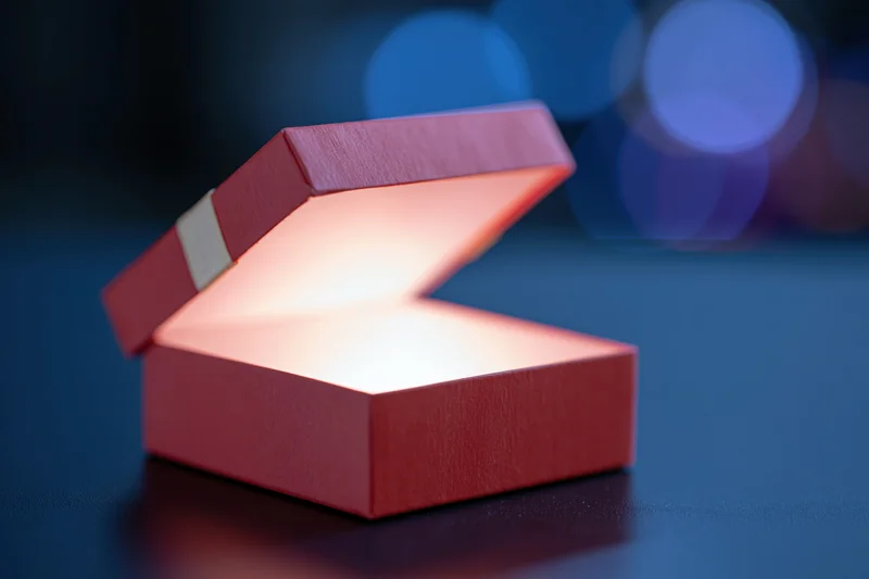 Open red gift box with glowing interior on reflective dark surface
