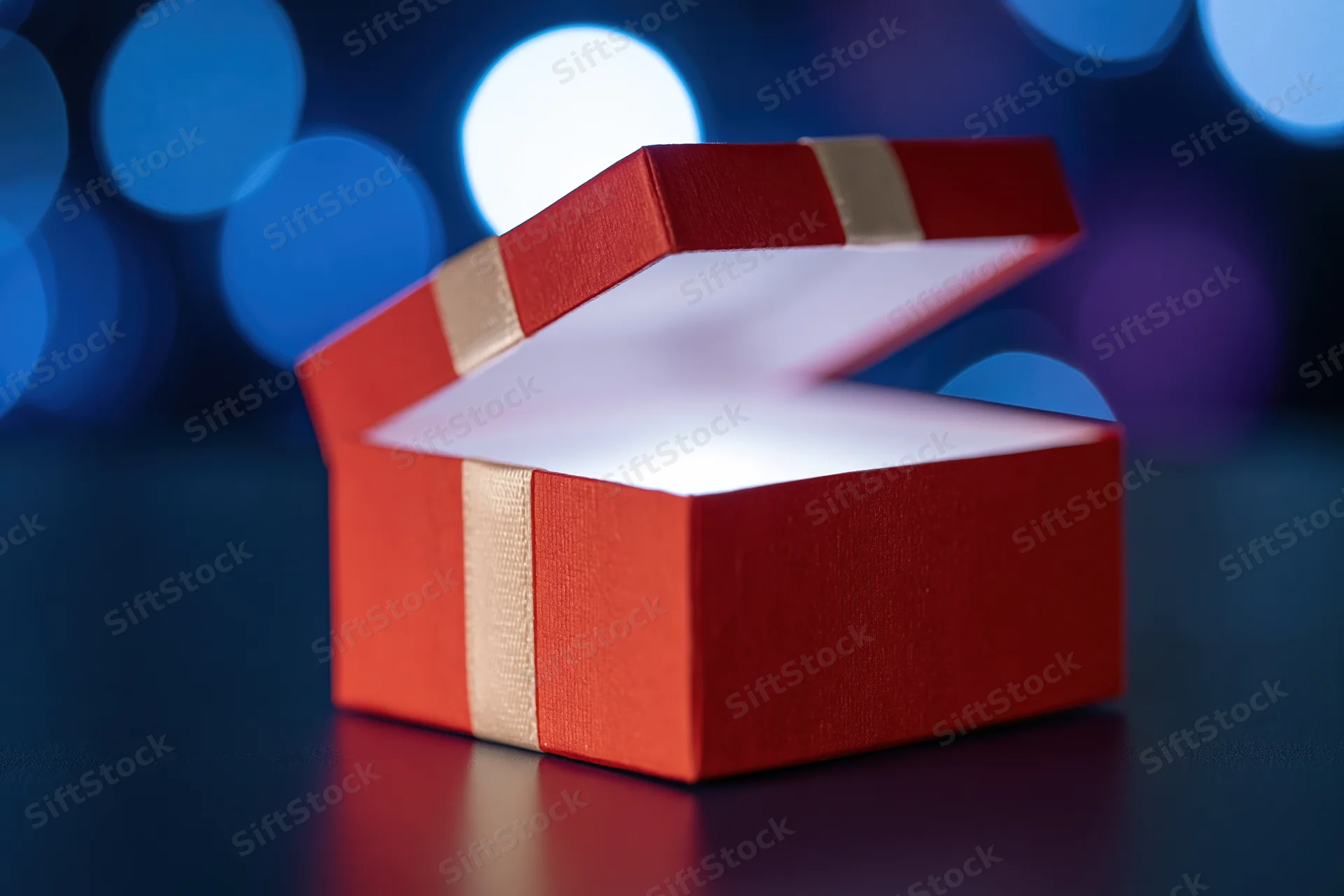 Open red gift box with lid ajar on reflective dark surface against blue bokeh background