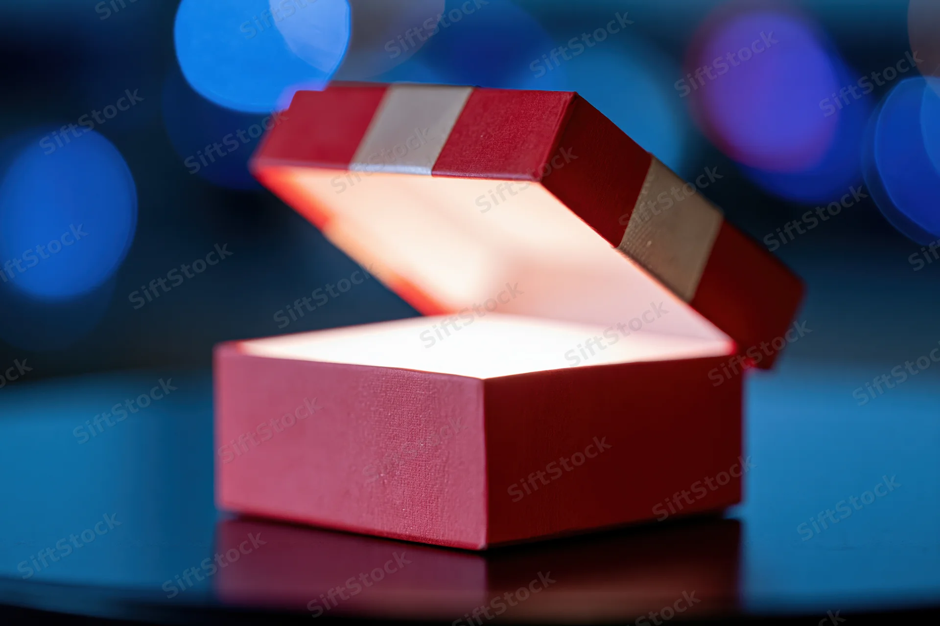 Open red gift box with glowing interior on reflective dark surface