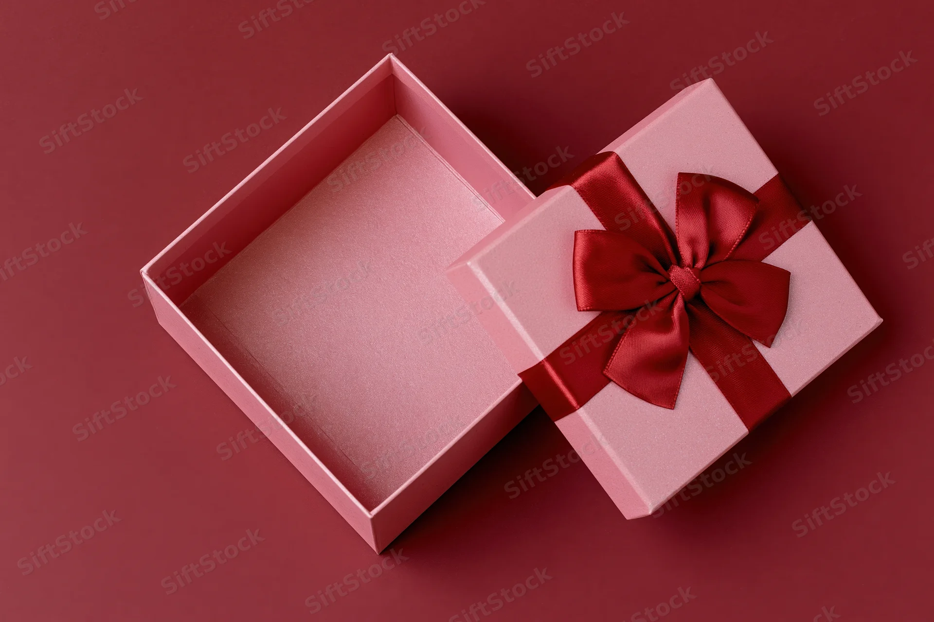 Open pink gift box with red satin bow on maroon surface