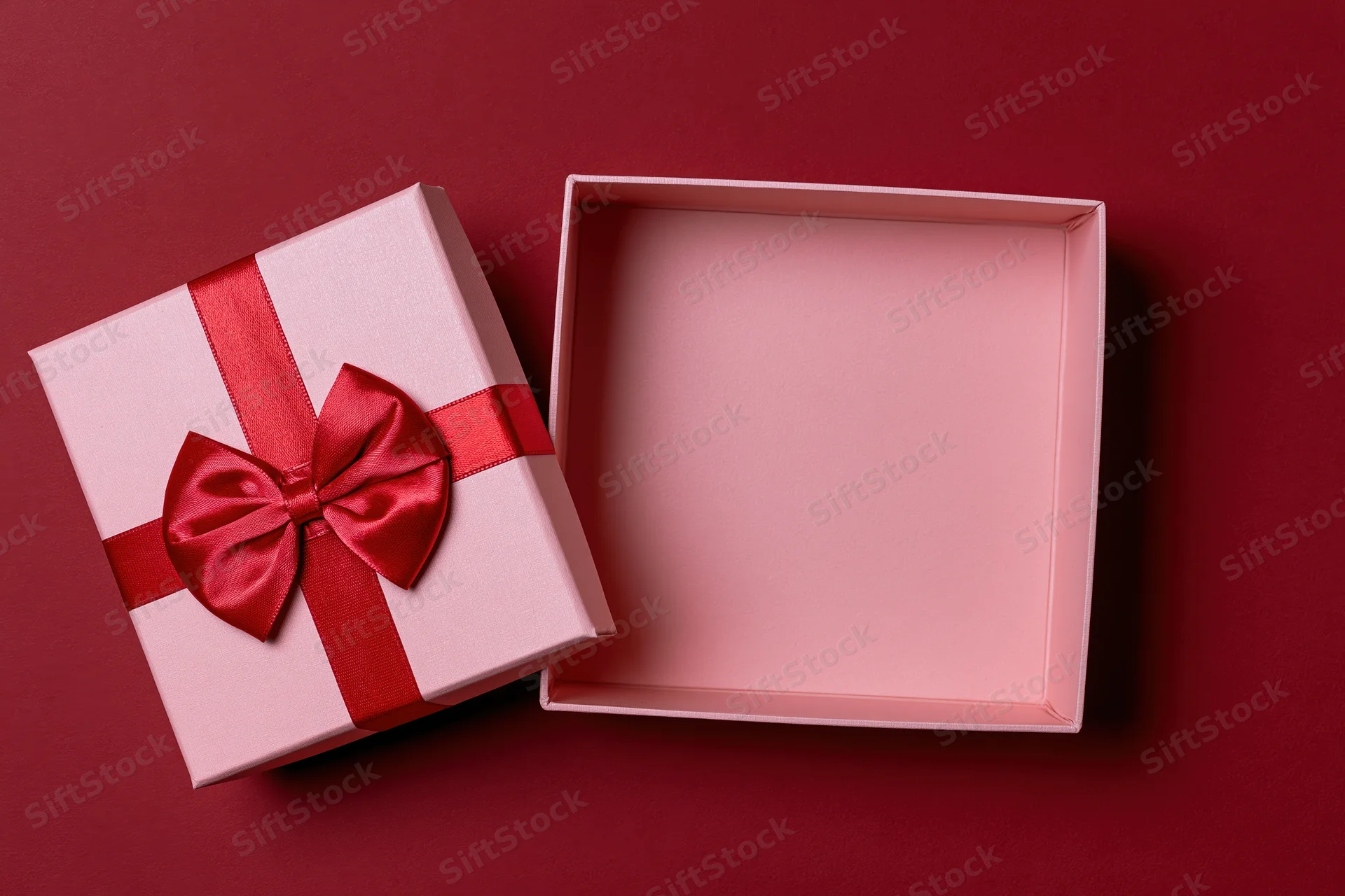 Open pink gift box with red satin bow on red background