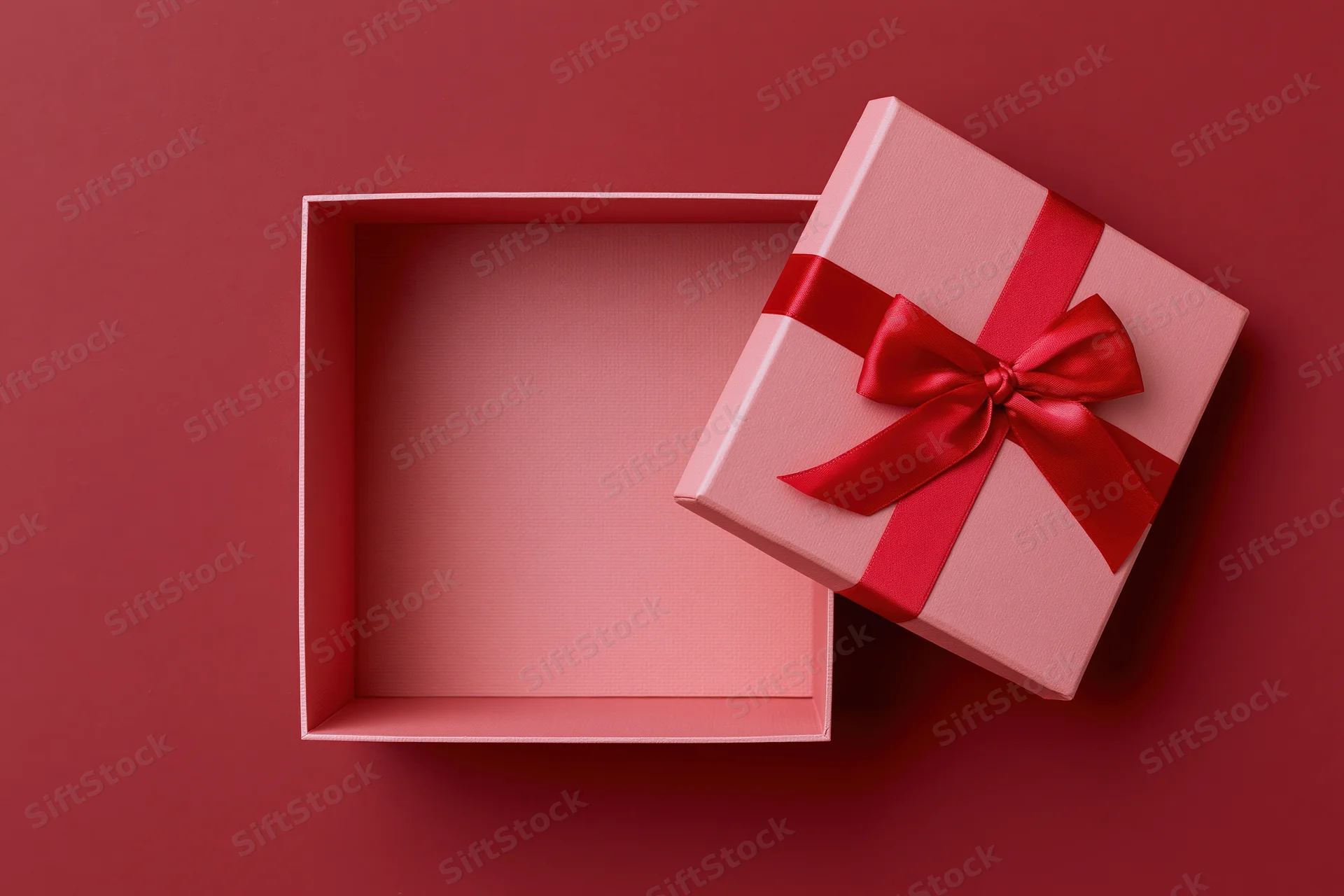 Open pink gift box with red satin bow on red surface
