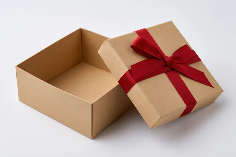 Open square kraft cardboard gift box with red ribbon bow on white background