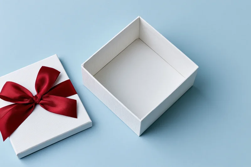 Open white gift box with red satin ribbon bow beside it on light blue surface