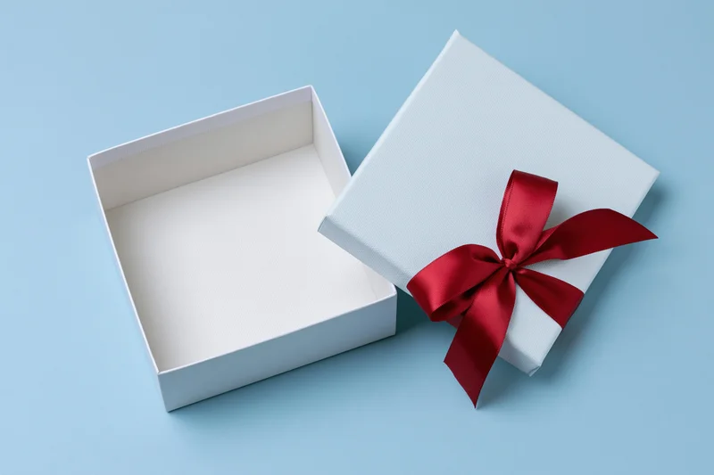 Open white gift box with red satin ribbon bow on blue background