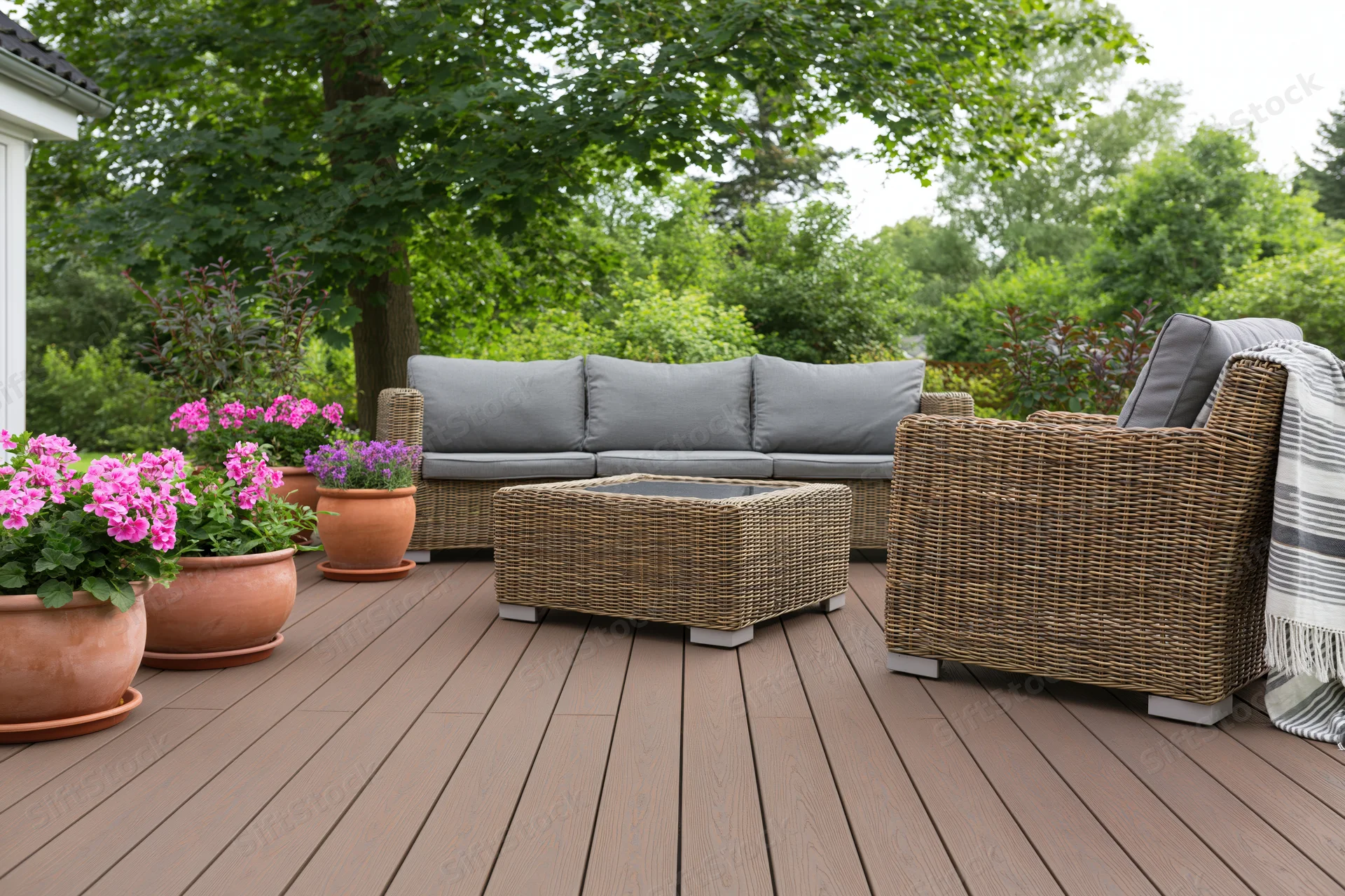 Wicker sofa and armchair with coffee table on a wooden deck surrounded by potted flowers and greenery