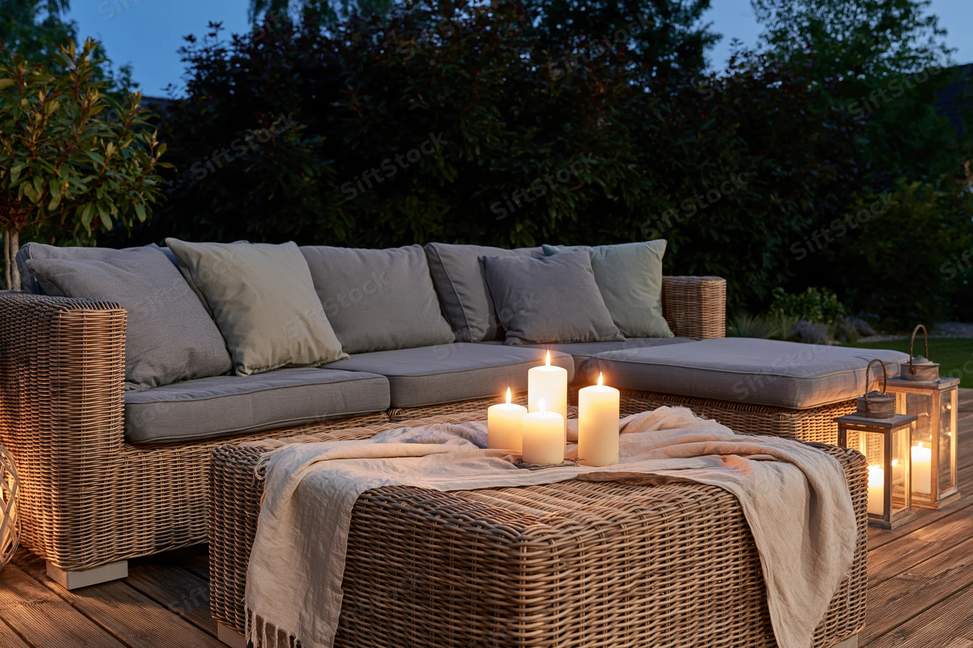 Wicker sectional sofa with candles and lanterns on a wooden deck at dusk