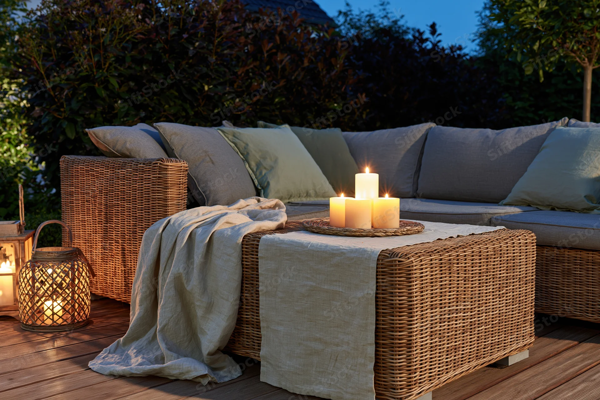 Wicker sectional sofa with candles and lanterns on a wooden deck at dusk
