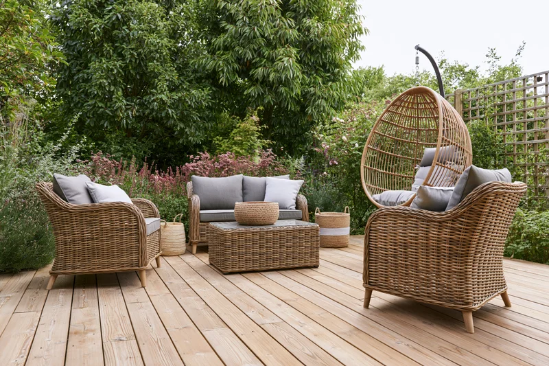 Wicker lounge furniture set arranged on a wooden deck surrounded by greenery