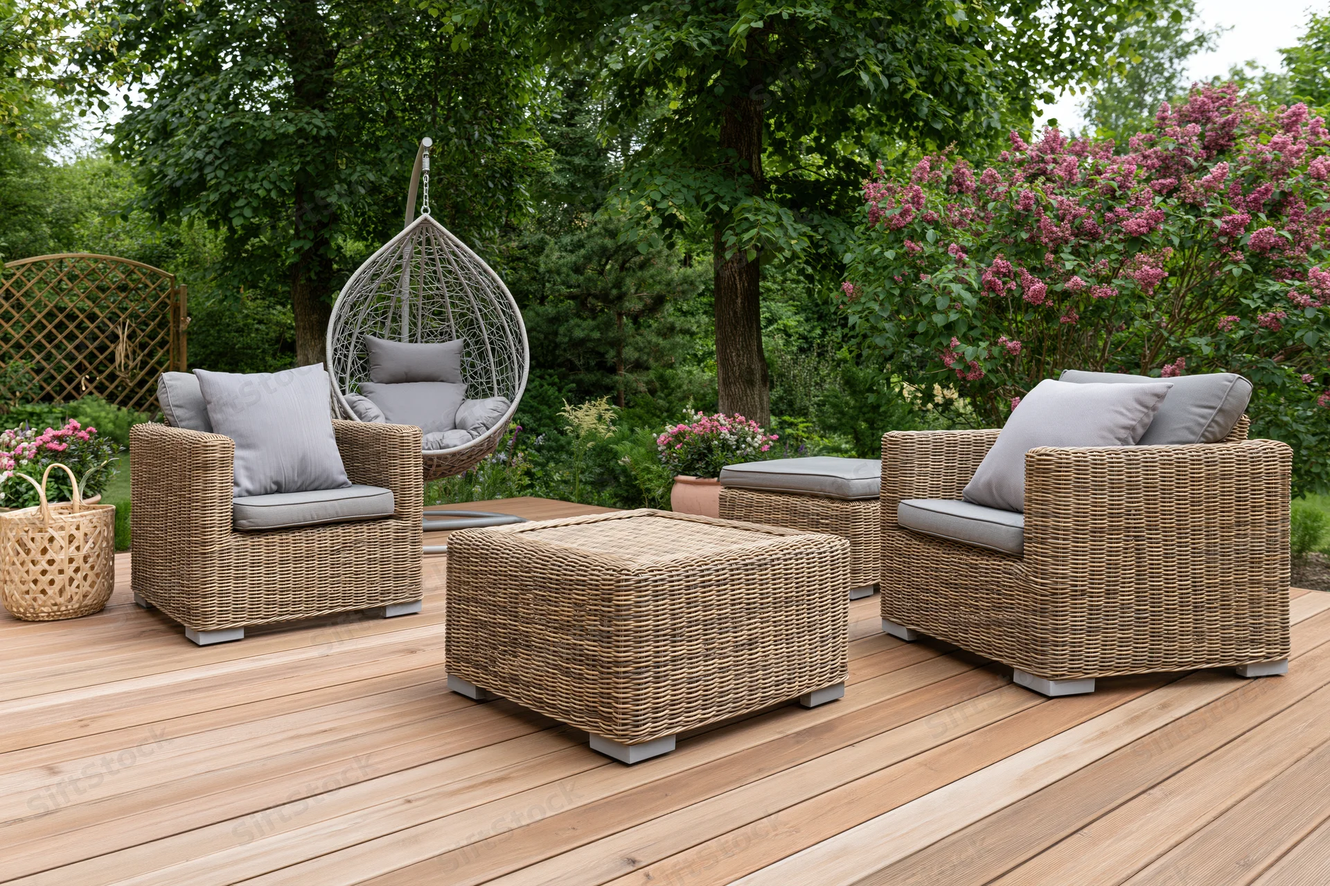 Wicker lounge chairs and ottoman arranged on a wooden deck surrounded by greenery and flowering shrubs