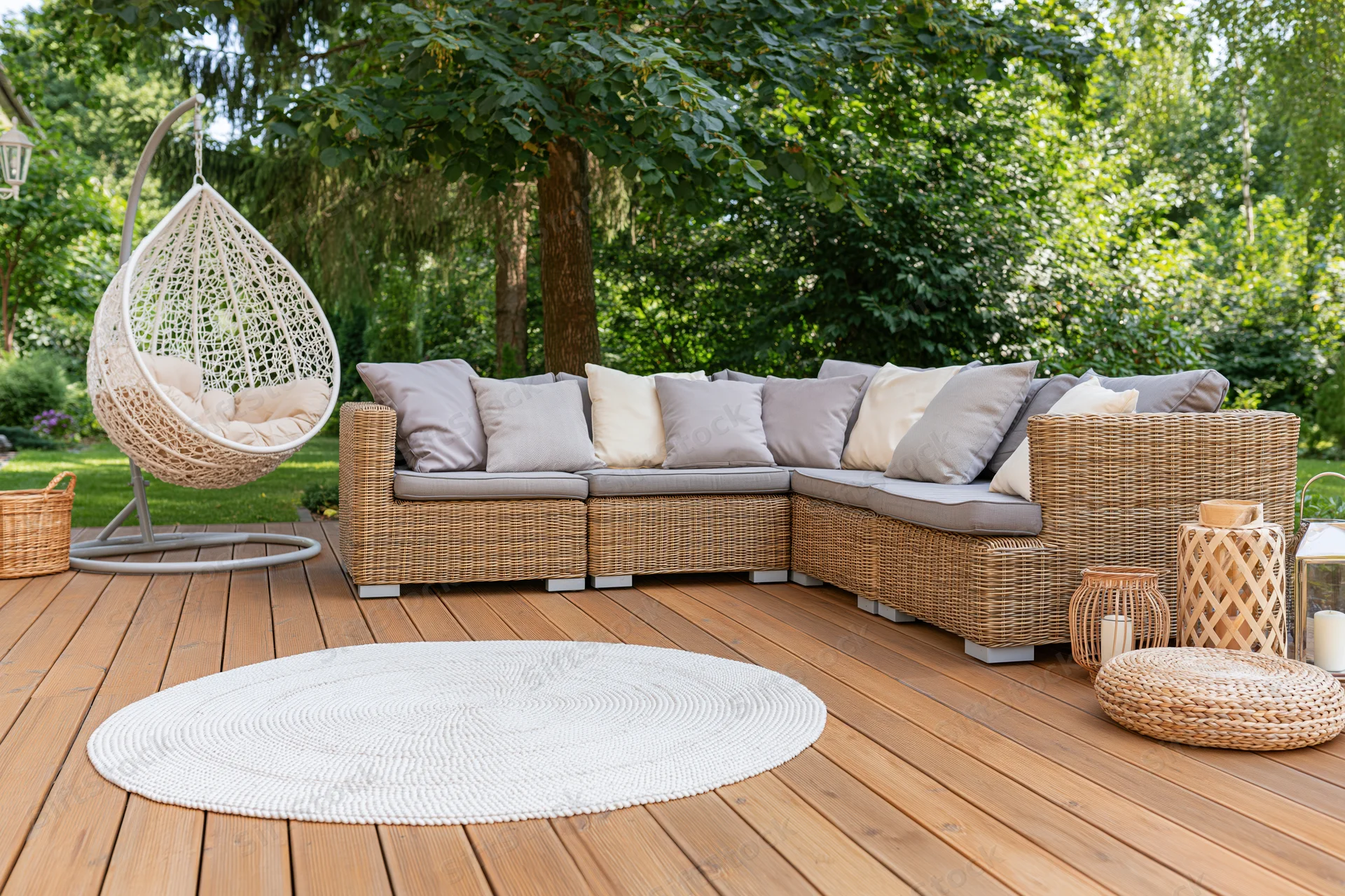 Wicker sectional sofa with cushions on wooden deck patio surrounded by greenery