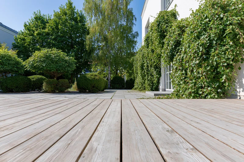 Wooden deck terrace leading to landscaped garden with ivy-covered house and trees
