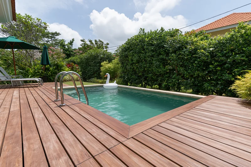 Small rectangular swimming pool in a private villa backyard with wooden deck and greenery