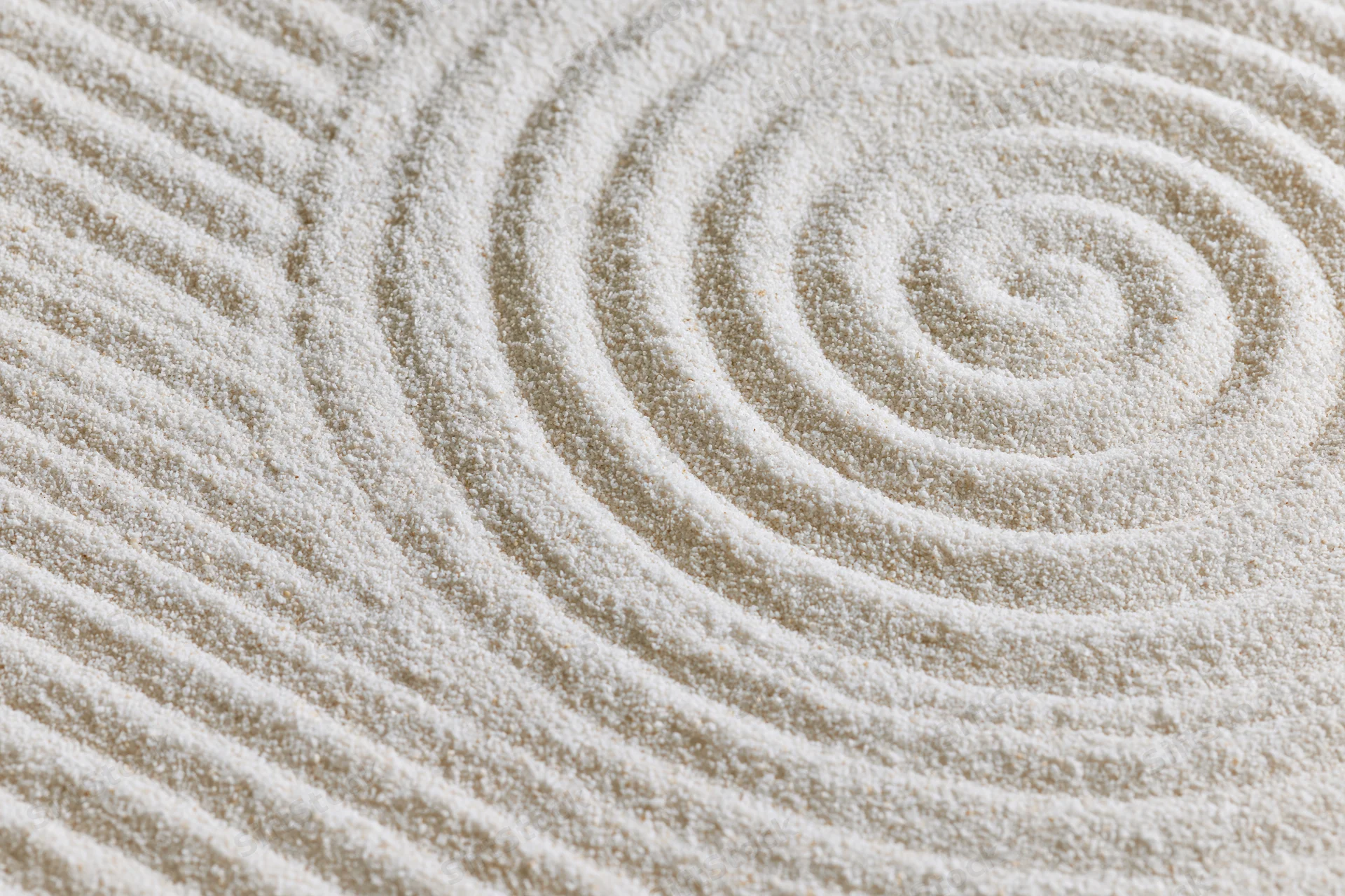 Raked sand surface with spiral and striped geometric patterns in a zen garden
