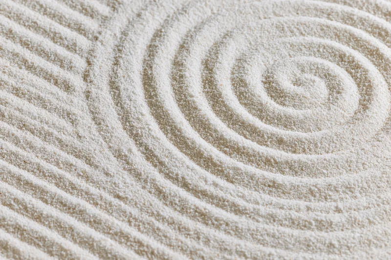 Raked sand surface with spiral and striped geometric patterns in a zen garden