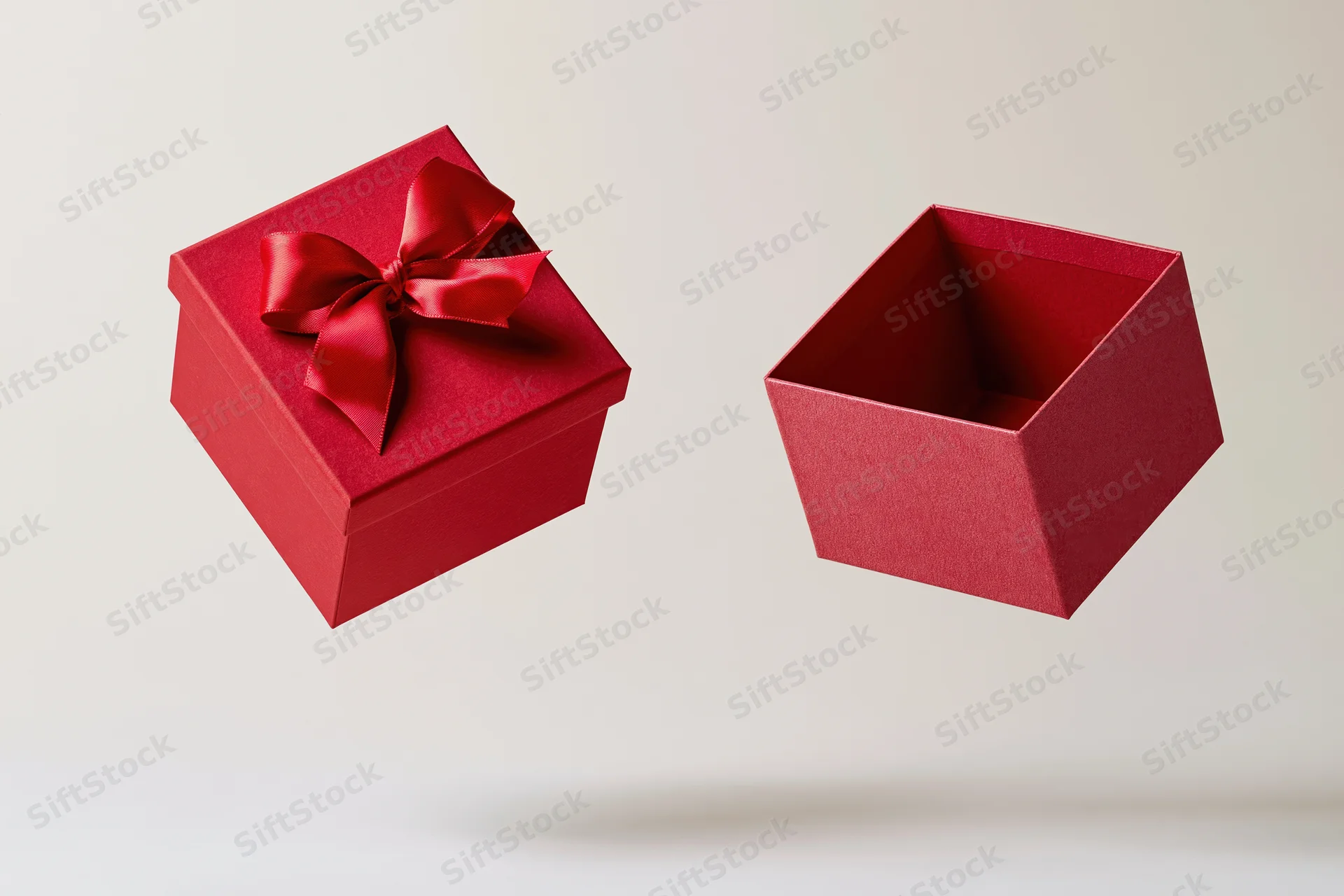 Red gift box with lid floating midair, one closed with satin bow, one open, against white background