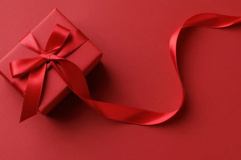 Red gift box with satin ribbon bow on red surface