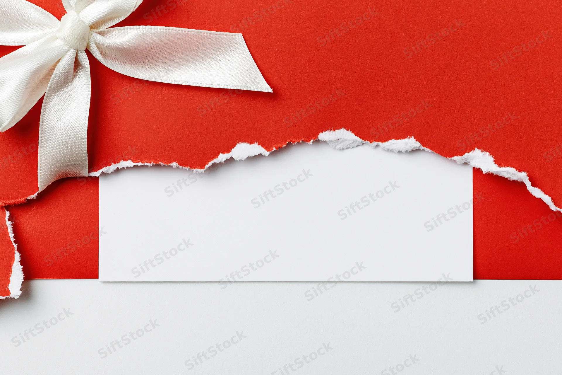 Torn red gift wrap with white satin bow revealing blank white label below