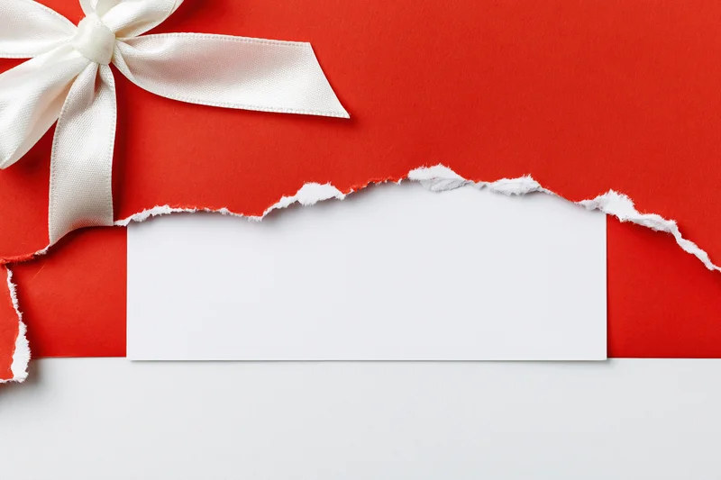 Torn red gift wrap with white satin bow revealing blank white label below
