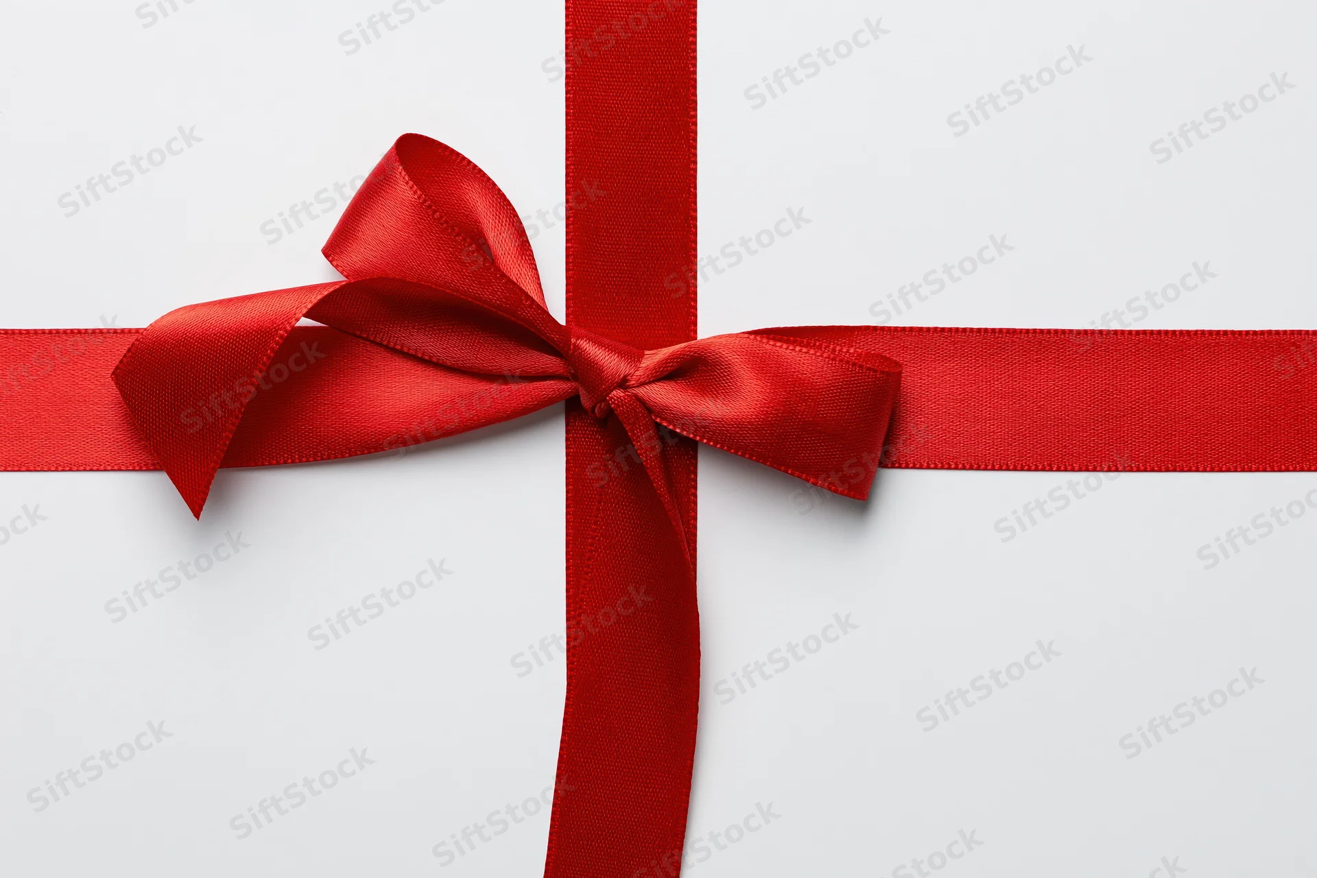 Red satin ribbon tied in a bow crossing horizontally and vertically on white background