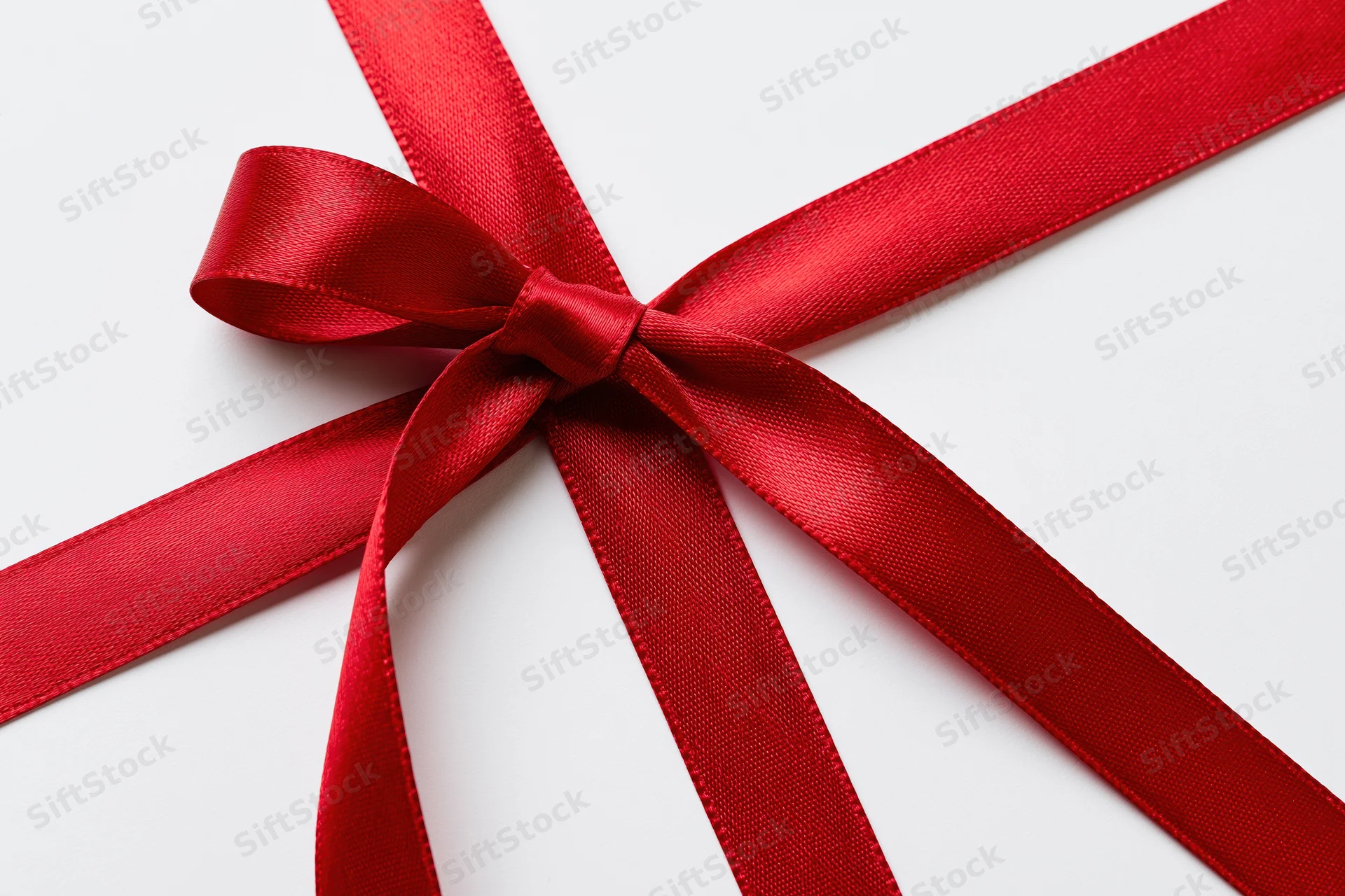 Red satin ribbon tied in a bow forming a cross shape on white background
