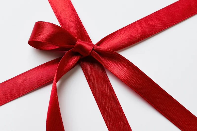 Red satin ribbon tied in a bow forming a cross shape on white background
