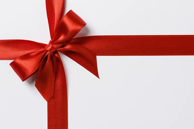 Red satin ribbon tied in a bow forming a cross shape on a white surface with copyspace