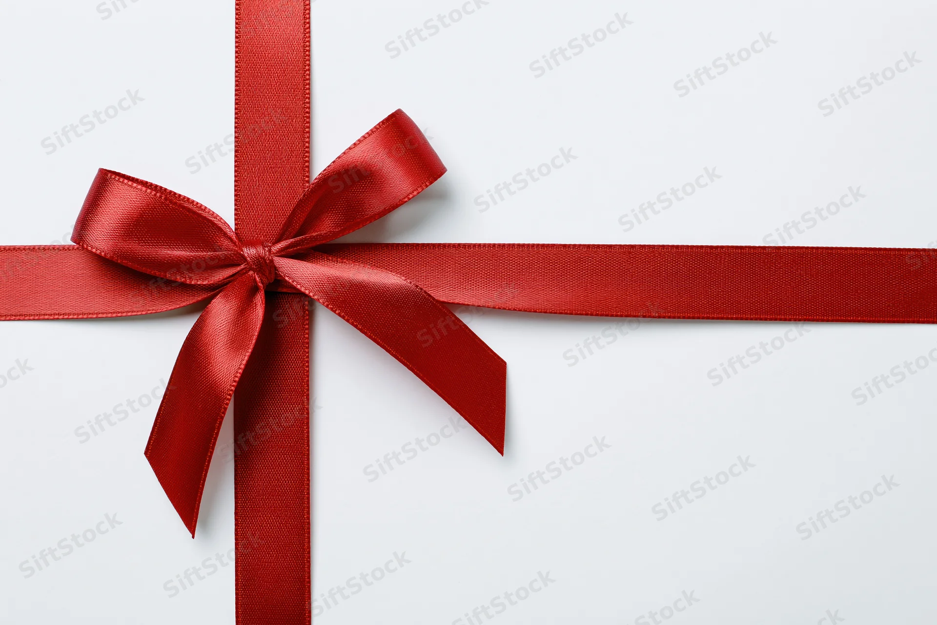 Red satin ribbon tied in a bow forming a cross on a white surface with copyspace