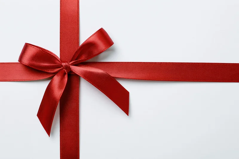 Red satin ribbon tied in a bow forming a cross on a white surface with copyspace