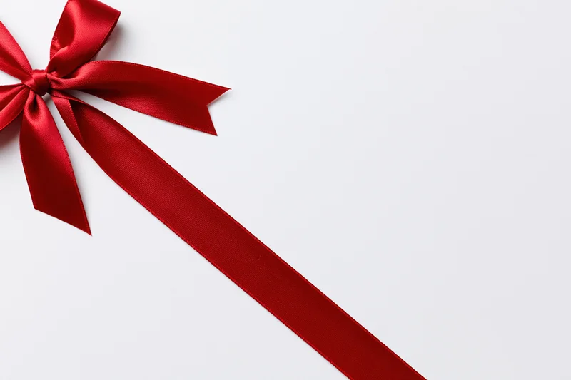 Red satin ribbon tied in a bow diagonally across a white background
