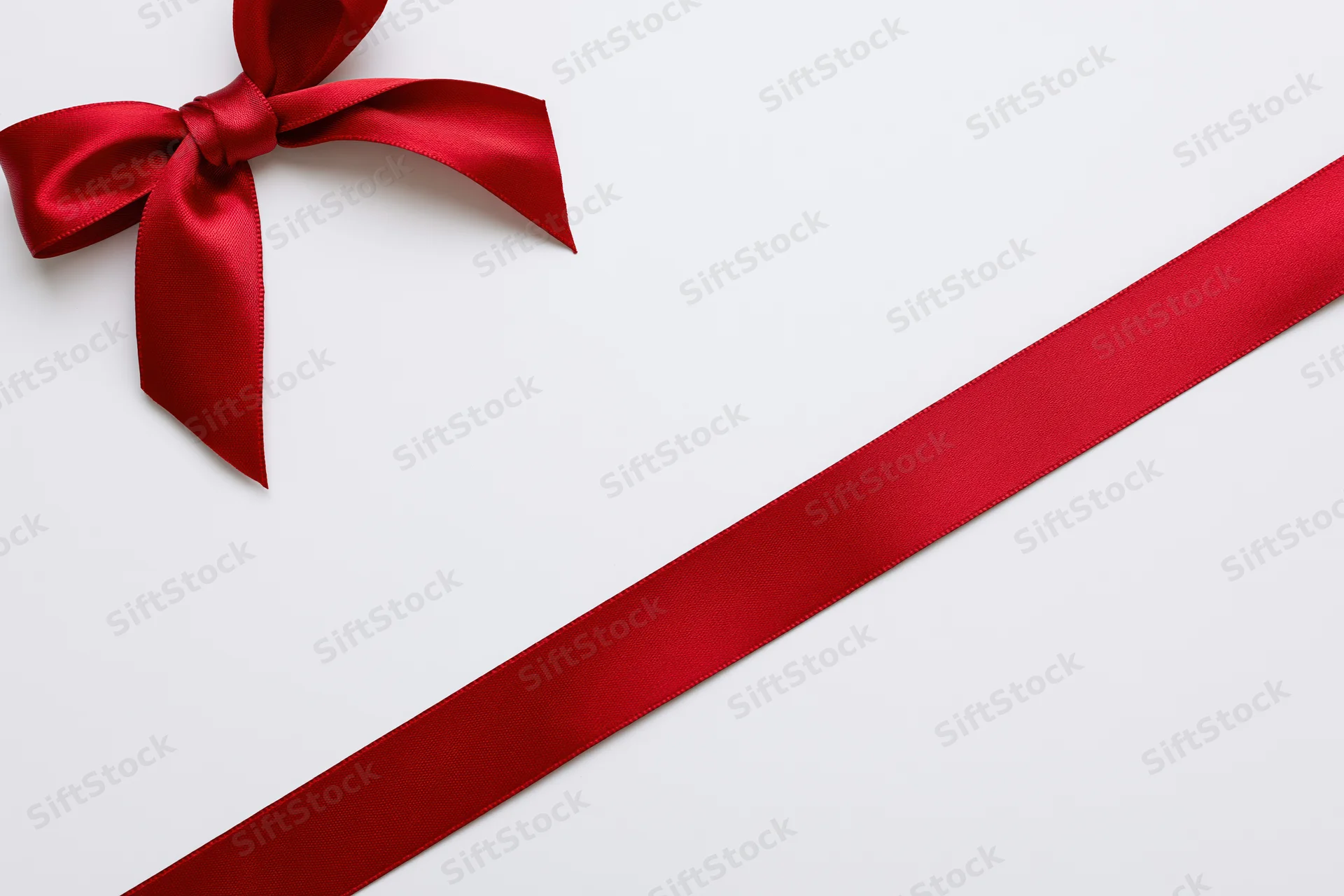 Red satin ribbon tied in a bow diagonally across a white surface