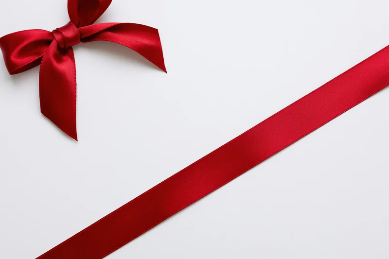 Red satin ribbon tied in a bow diagonally across a white surface