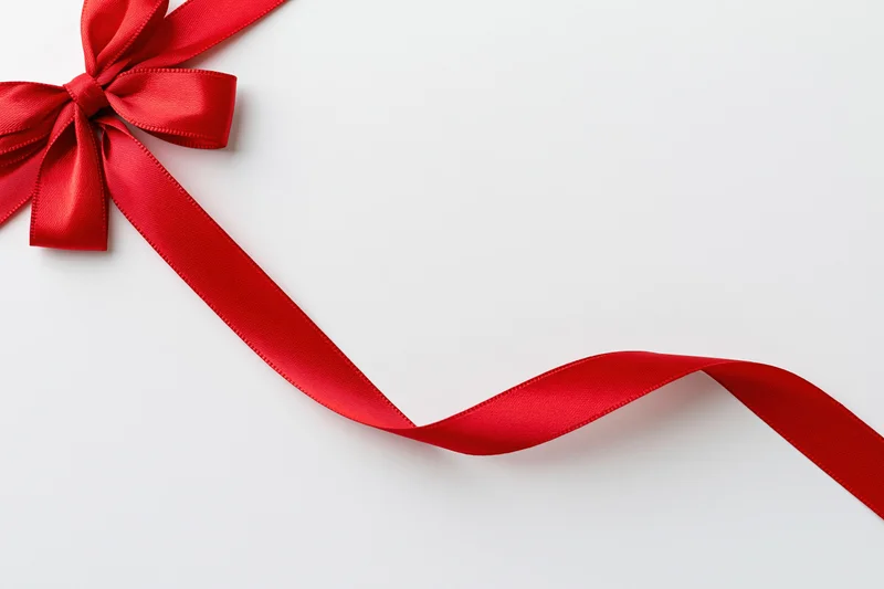 Red satin ribbon tied in bow running diagonally across white background