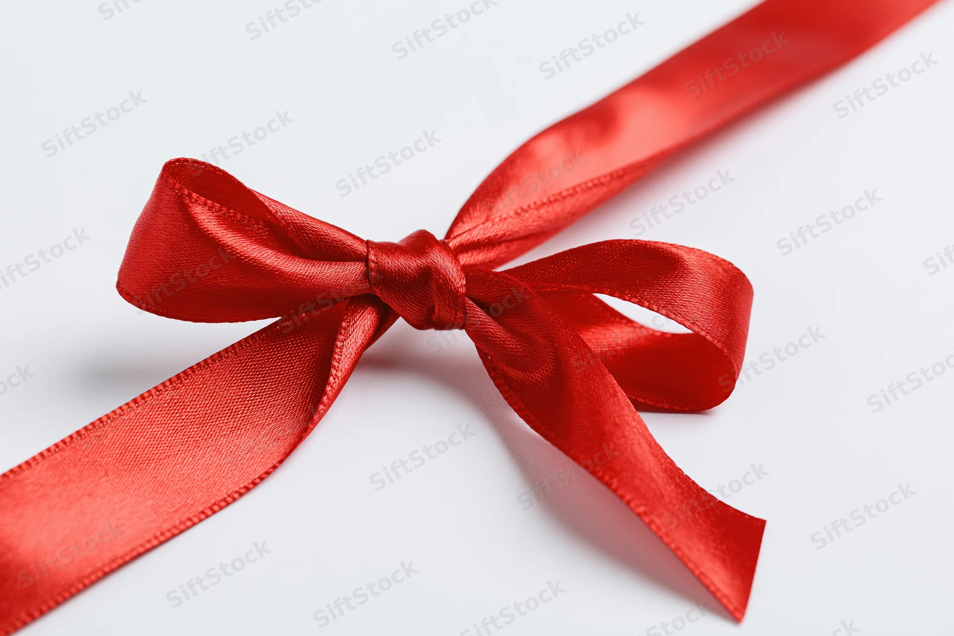 Red satin ribbon tied in a bow crossing diagonally on white background