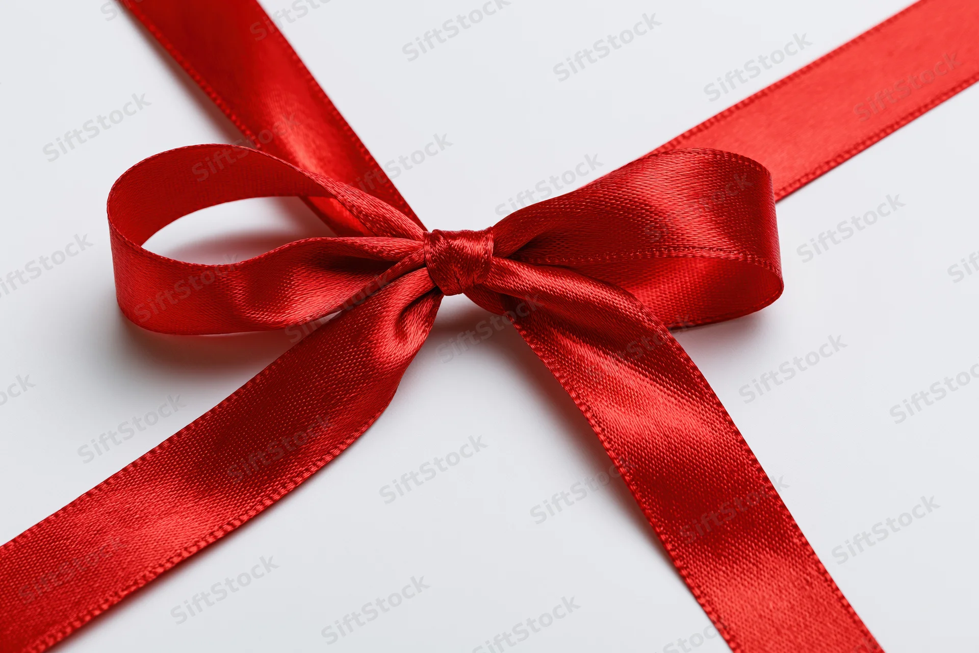 Red satin ribbon tied in a neat bow crossing diagonally on white background