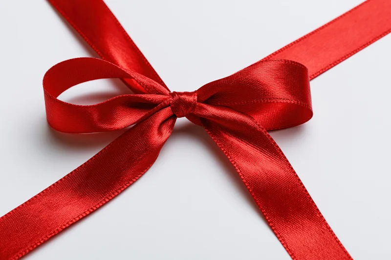 Red satin ribbon tied in a neat bow crossing diagonally on white background