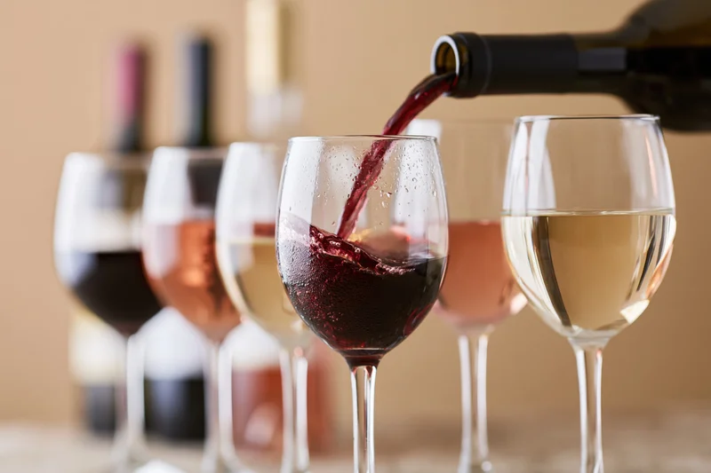 Red wine being poured into a glass among a row of wine glasses on a table