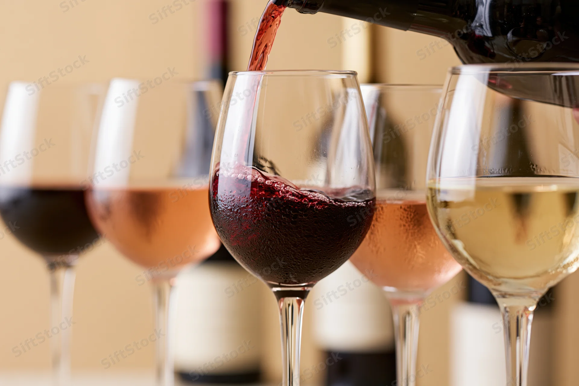 Red wine being poured into a glass with other wine glasses in a row on a table