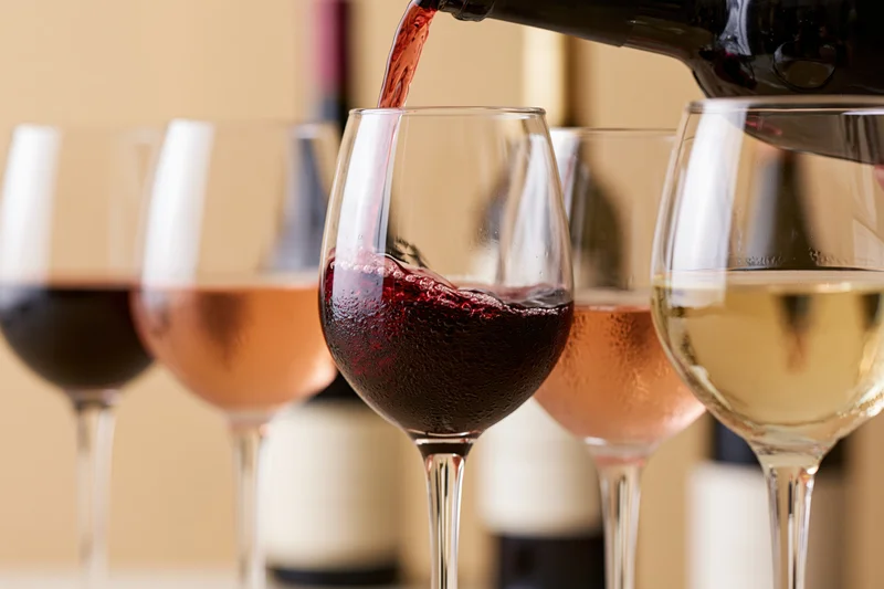 Red wine being poured into a glass with other wine glasses in a row on a table
