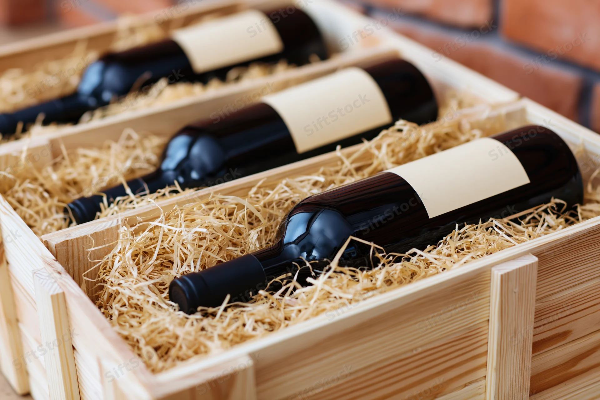 Red wine bottles lying horizontally in a wooden crate filled with straw