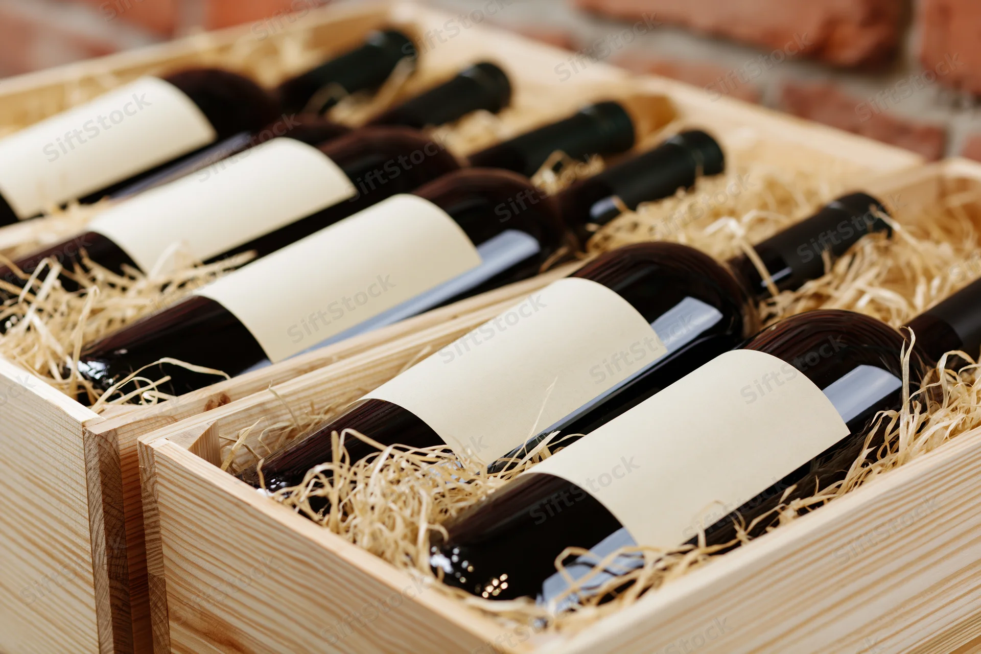 Red wine bottles lying horizontally in wooden crates filled with straw for gift presentation
