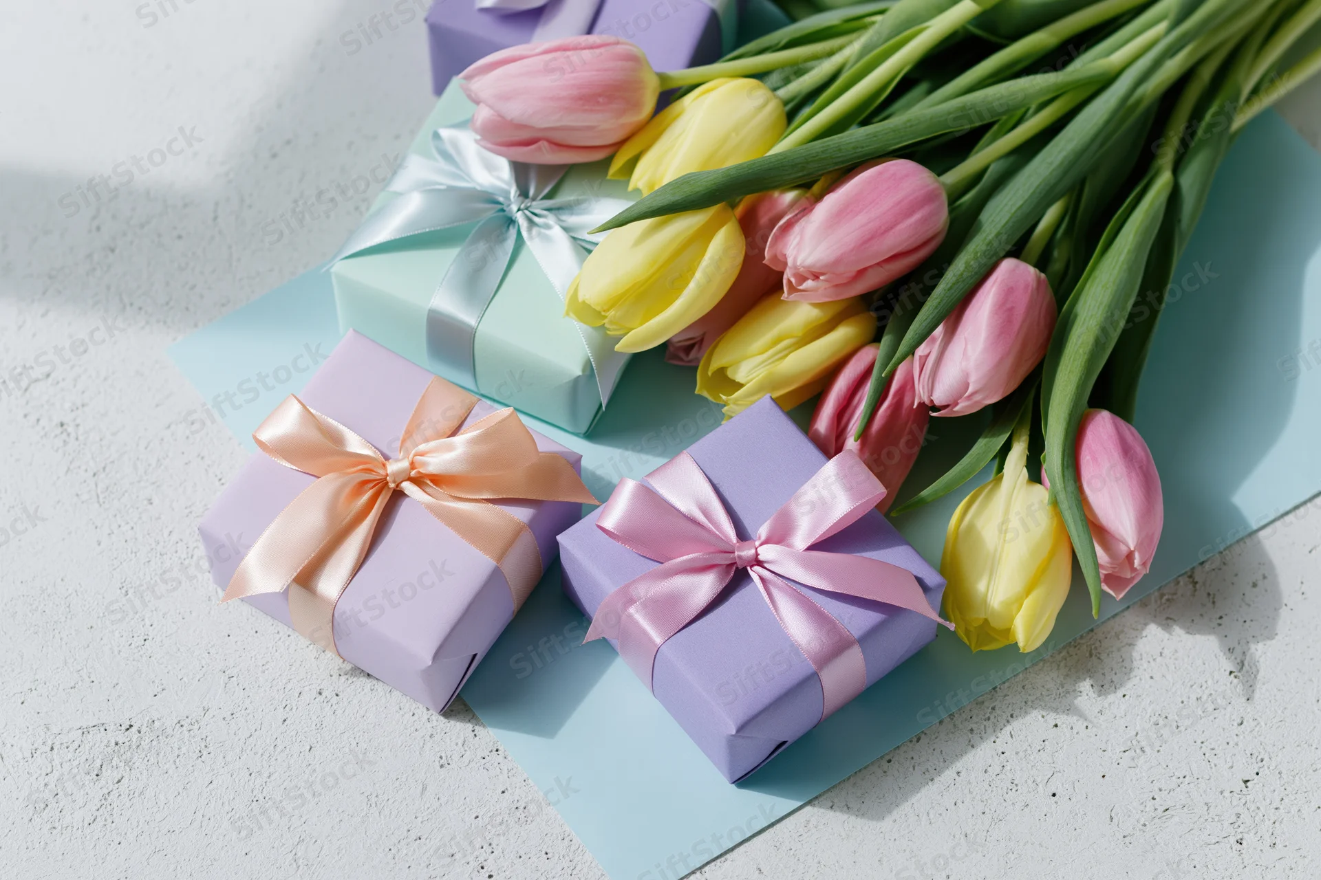 Pastel-wrapped gift boxes with satin ribbon bows and tulip bouquet arranged on light surface