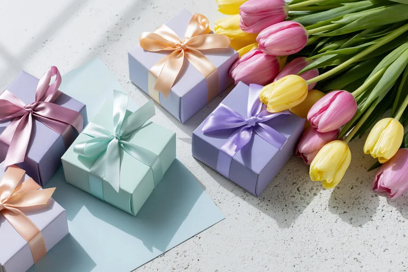 Pastel gift boxes with satin ribbon bows and tulips on a light surface