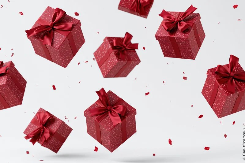 Red gift boxes with satin ribbon bows floating in midair against white background with scattered confetti