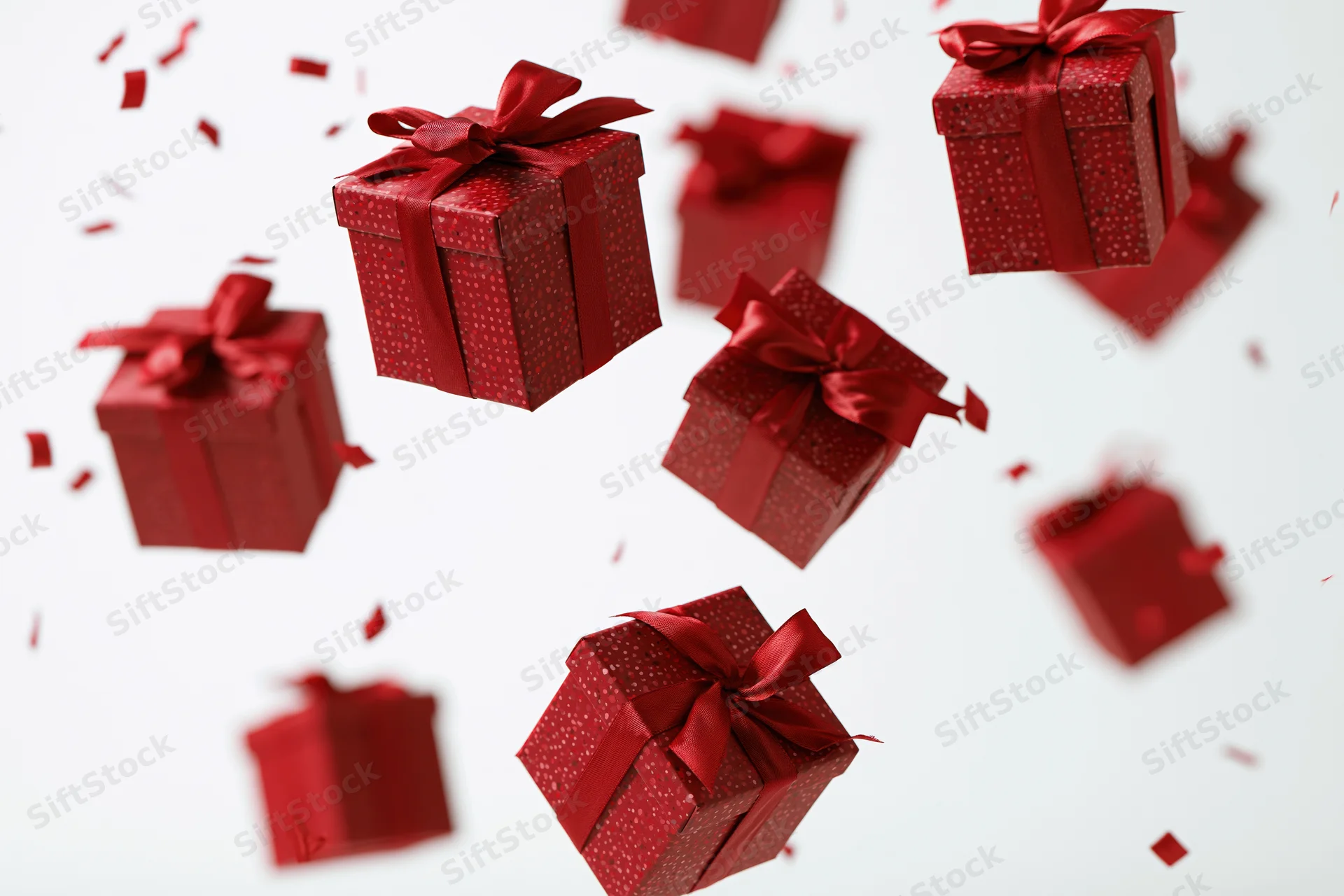 Red gift boxes with satin ribbon bows floating and tumbling in midair against white background with scattered confetti